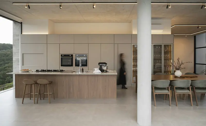 Modern open-plan kitchen with a timber-clad island, bar stools and a dining table beside large windows